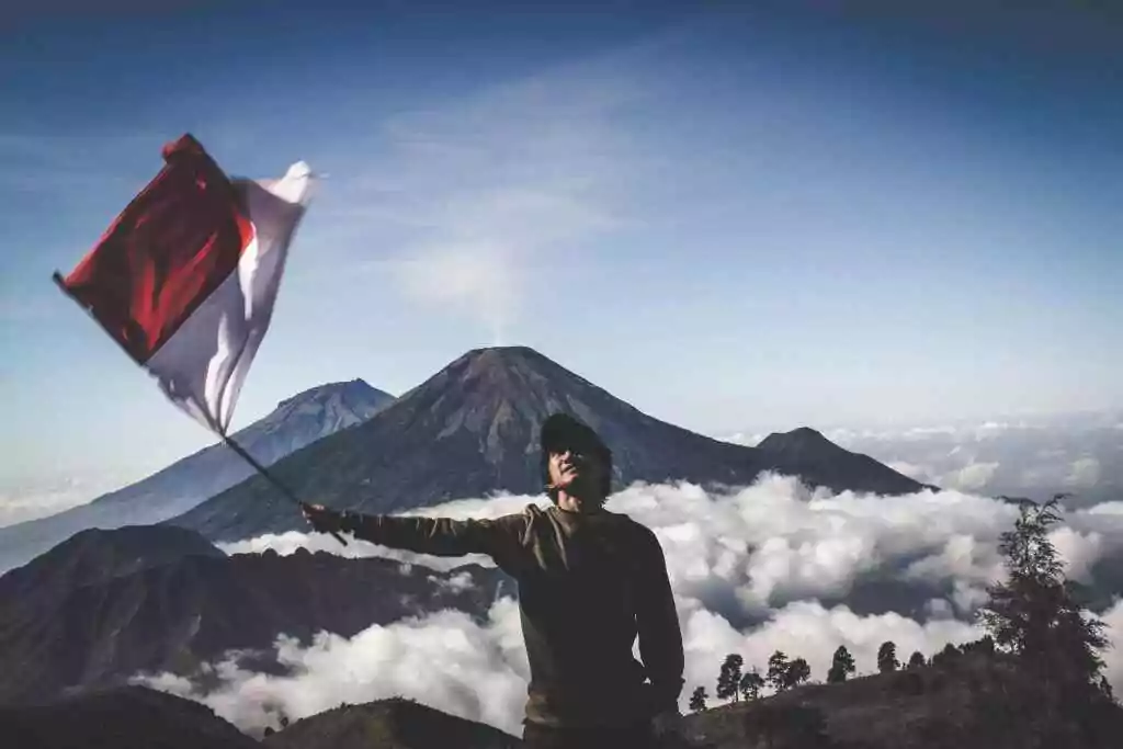 Your World Awaits: 15+ Visa-on-Arrival Countries for UAE 31 A hiker waves the Indonesian flag atop a scenic mountain, surrounded by clouds.