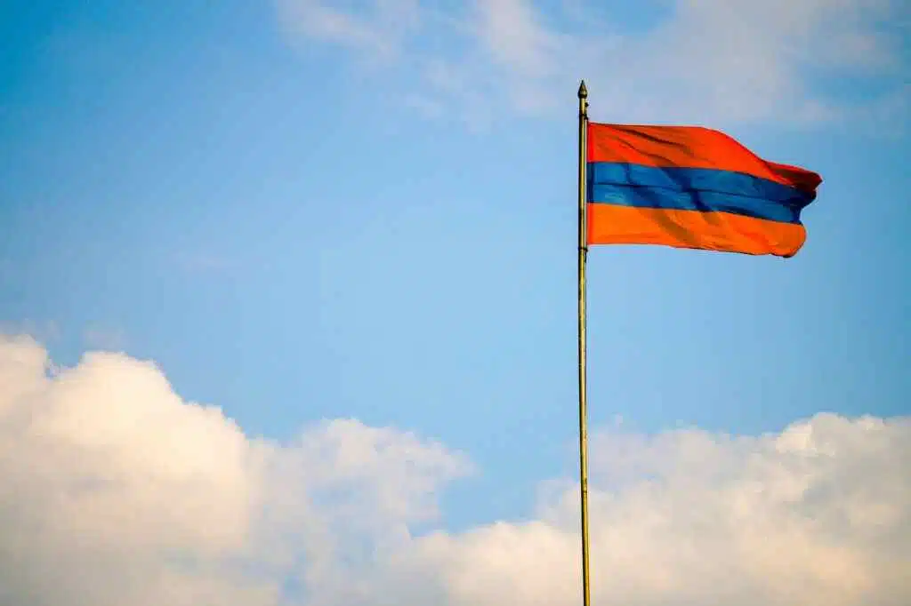 Armenia Visa for UAE: How to get it? 6 Armenian flag on a flagpole swaying in the windy blue sky with clouds.