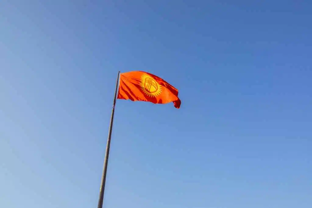 Your World Awaits: 15+ Visa-on-Arrival Countries for UAE 19 Red national flag of Kyrgyzstan waving on a flagpole under a clear blue sky.