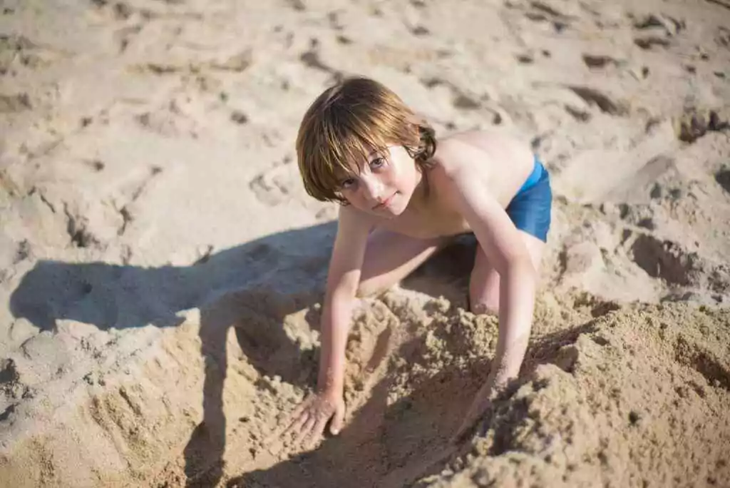 Barasti Beach: Free Entry or Pay? 2 A young boy in blue shorts playing in the sand on a sunny beach day.