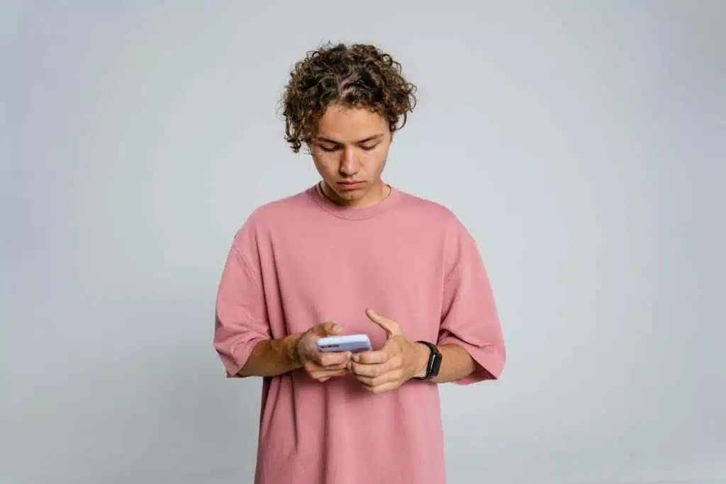 NBAD Balance Inquiry UAE – 7 No-Fee Methods in 2025 22 Teenage boy in pink shirt focuses on smartphone against gray background.