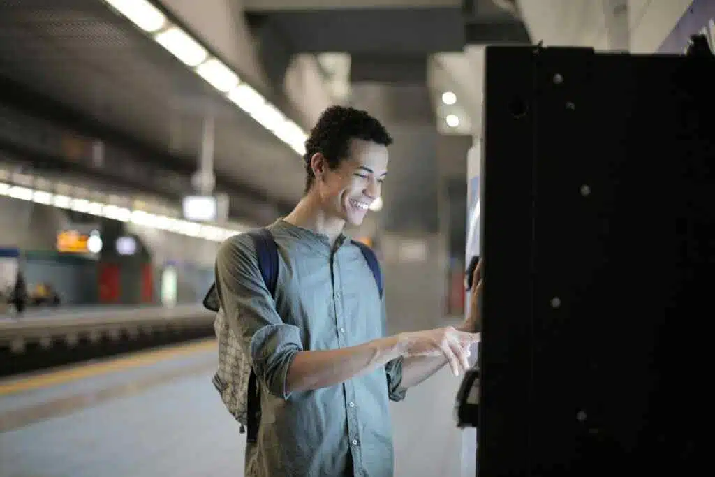 Al Ansari Balance Check: Instantly View Card Balance (2025) 22 Joyful young African American male in casual clothes with backpack focusing and interacting with vending machine at underground station against blurred railway platform