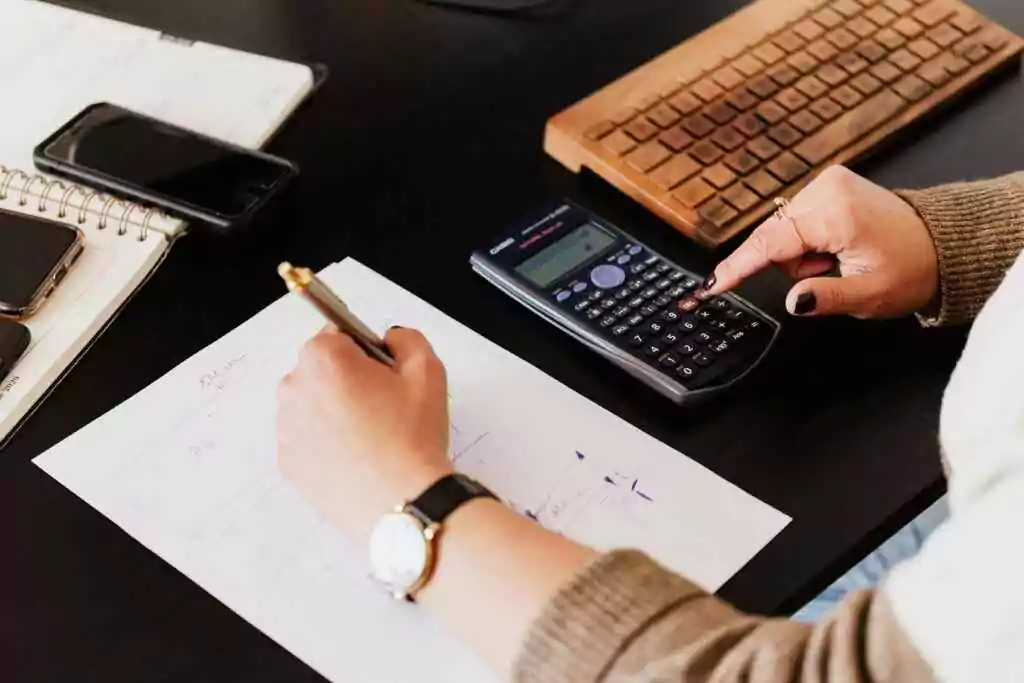 UAE Gratuity Calculation for Limited and Unlimited Contracts Close-up of hands working with a calculator and notebook on a desk, analyzing documents.