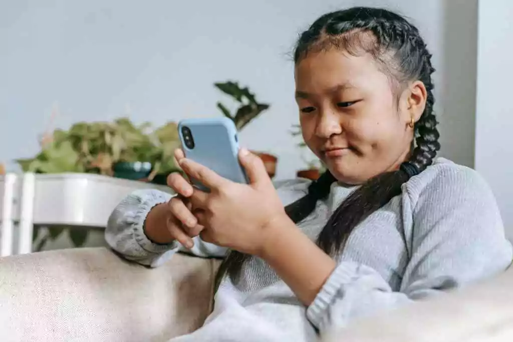 Never Overpay: 5 Free Ways to Check Lulu Salary (2025)! 18 A young girl with braided hair using a smartphone on a couch, illustrating digital pastime.