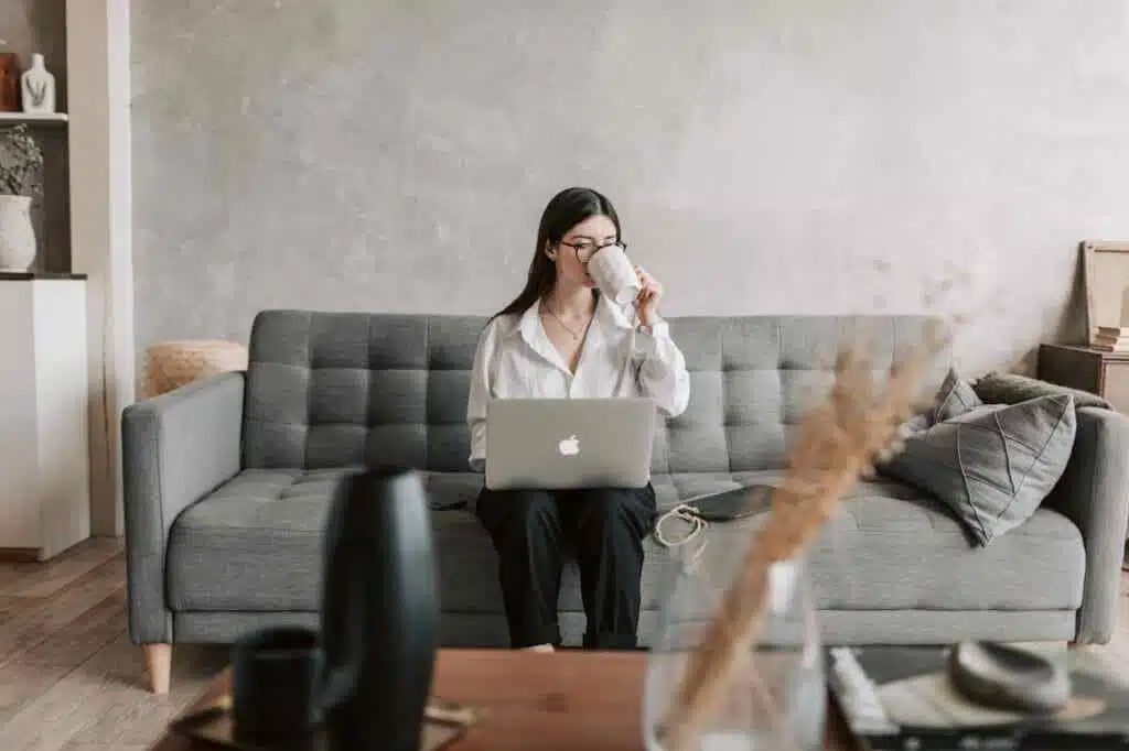 A woman sitting on a couch and having a tea while using a laptop