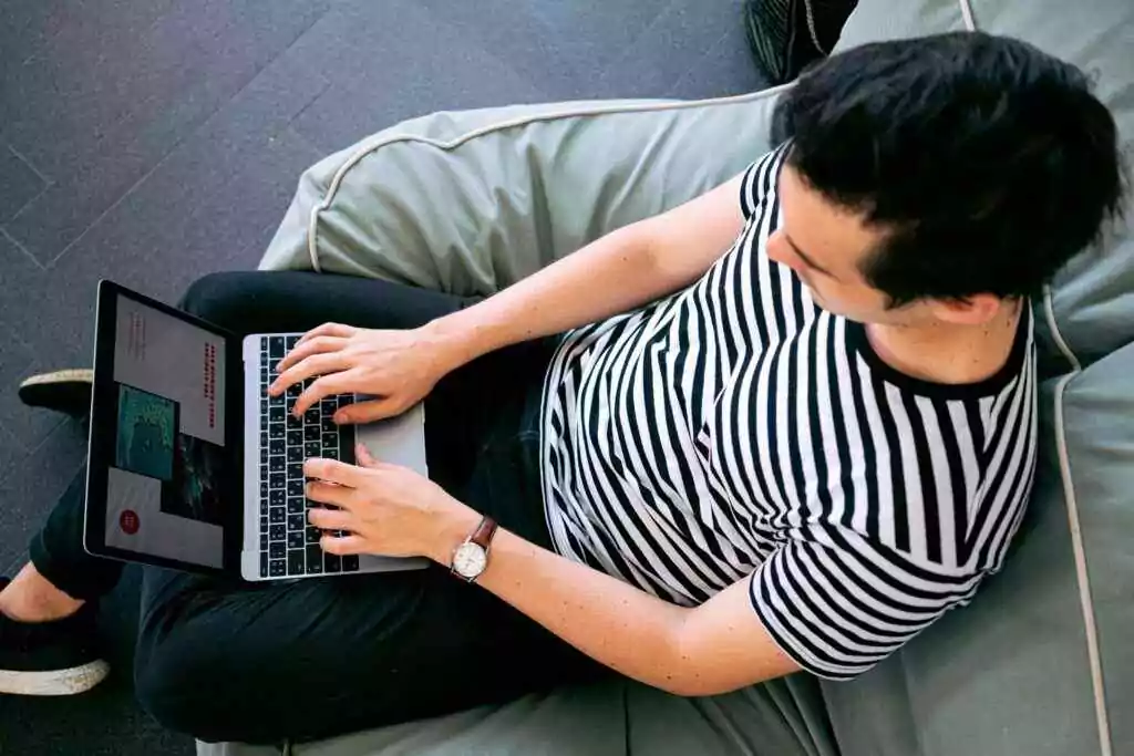 رجل يرتدي قميصًا مخططًا يستخدم جهاز كمبيوتر محمول على كيس فول، يجسد الإنتاجية المريحة.