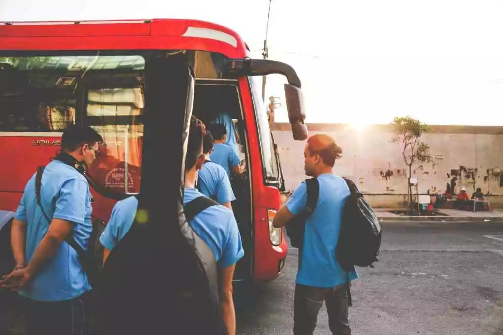 Musicians boarding a red bus in Tân Bình, Hồ Chí Minh City during sunrise. A lively street scene.