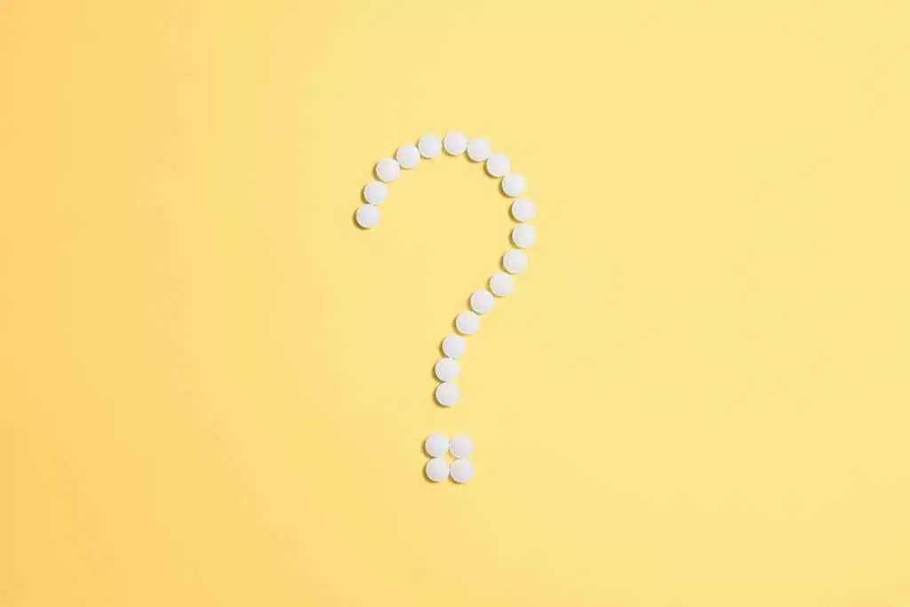 White pills arranged into a question mark shape on a vibrant yellow background.