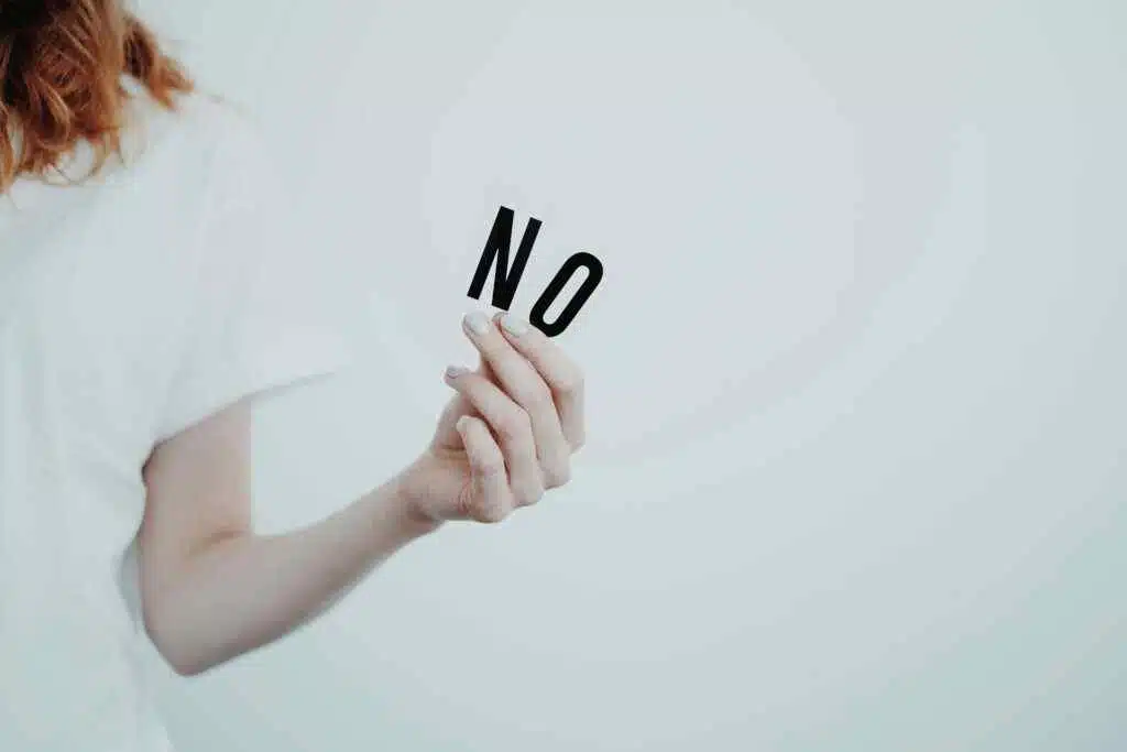 لقطة مقربة لشخص يحمل كلمة "لا" بأحرف سوداء على خلفية بيضاء ، ينقل رسالة رفض.