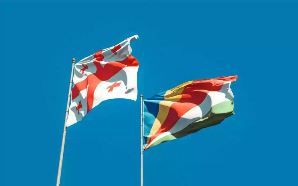 Vibrant image of Georgia and Seychelles flags waving with blue sky backdrop, symbolizing unity and cultural pride.