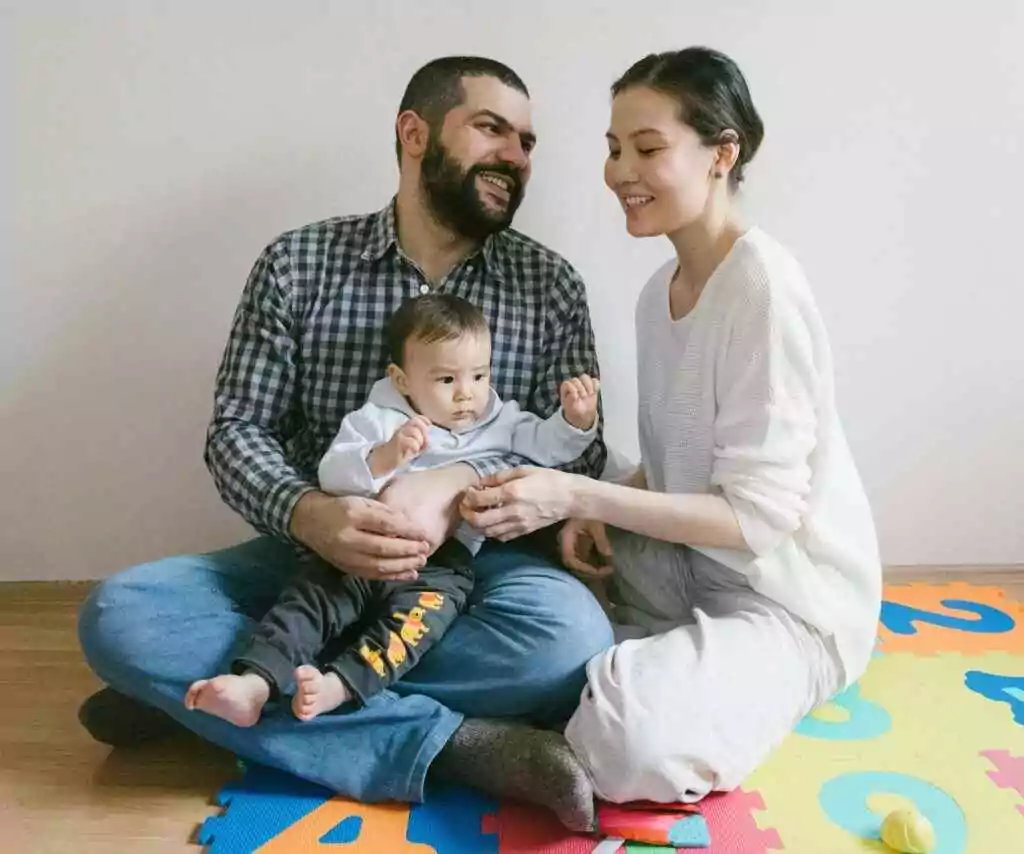 A joyful family with parents and baby enjoying playtime together indoors on a colorful puzzle mat.