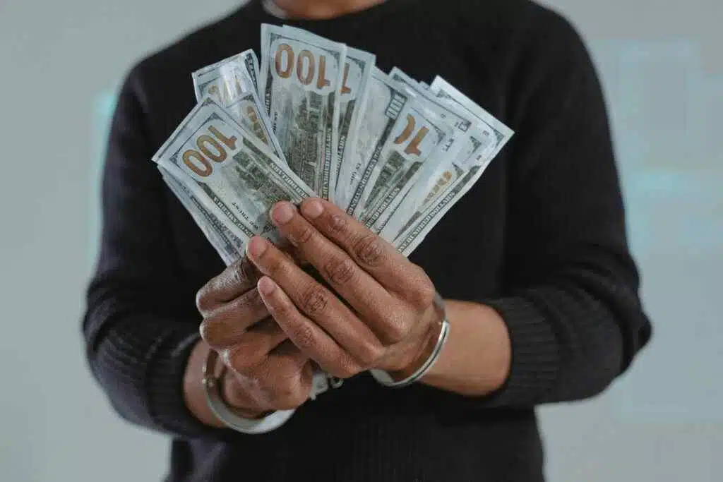 Close-up of hands holding 100-dollar bills while handcuffed, symbolizing crime and punishment.