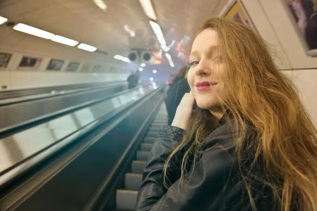 A young woman smiles on an escalator in a Budapest metro station, capturing modern urban life.