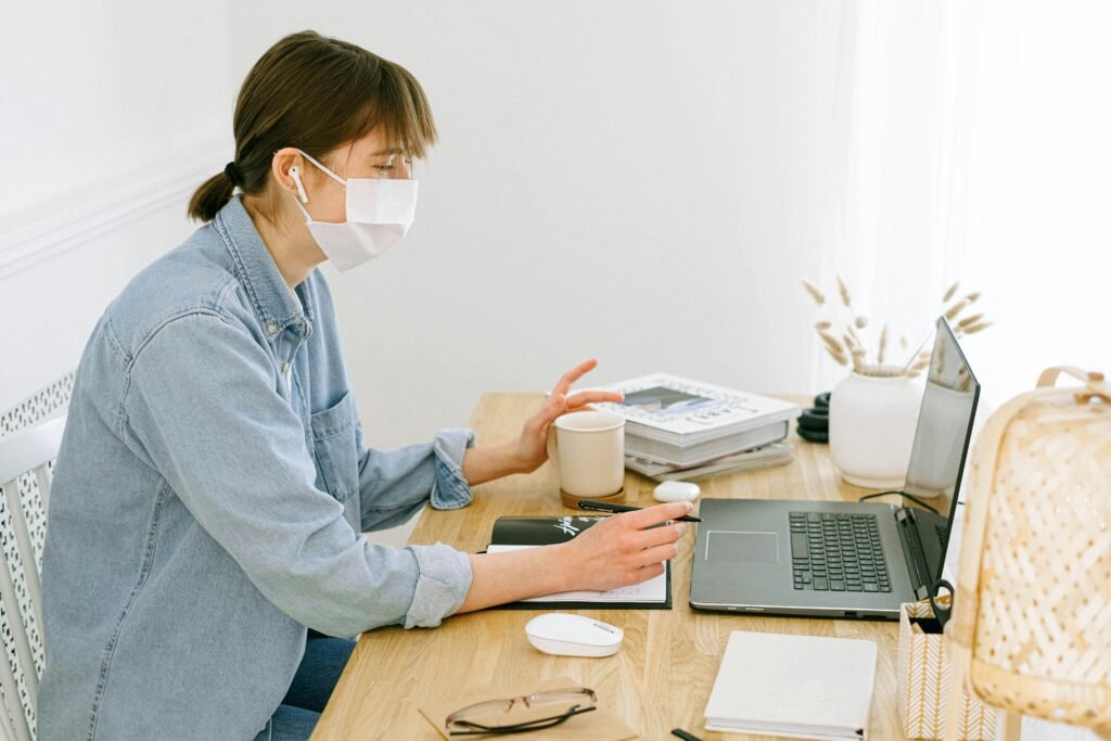 Woman wearing a face mask working from home with laptop and coffee.