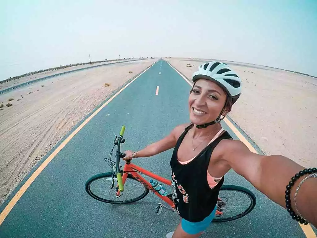 Young woman cycling on a desert road in Dubai, enjoying fitness and leisure.