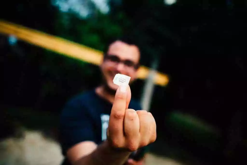 Portrait of a man smiling and holding a SIM card outdoors with focus on the hand.