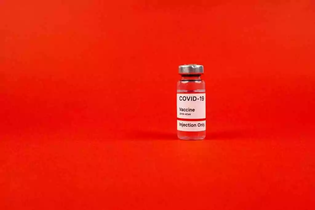 Glass vial of COVID-19 vaccine on a vibrant red backdrop, emphasizing protection.