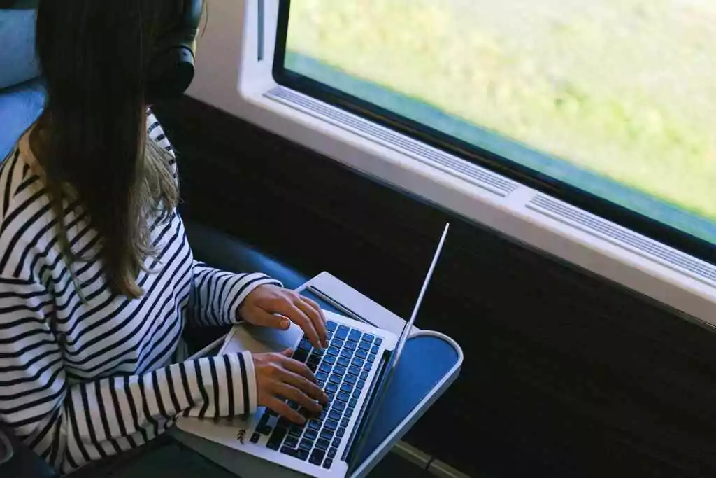 Person with headphones using laptop on a train, symbolizing remote work and digital nomad lifestyle.