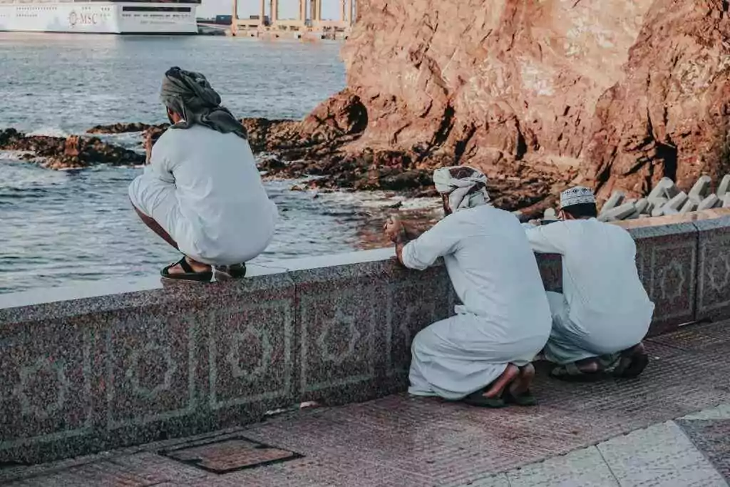 Omani men dressed traditionally, reflecting, by the seaside in Muscat, Oman.