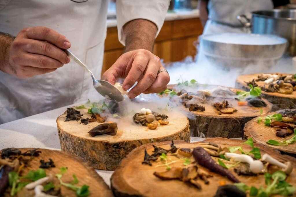 Where to Eat Cheap in Abu Dhabi? 5 Best Affordable Spots! 10 A chef artfully plating a gourmet dish with mushrooms and greens on wood slices.
