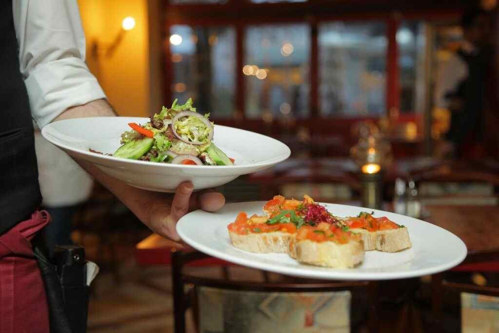 Where to Eat Cheap in Abu Dhabi? 5 Best Affordable Spots! 8 A waiter serves a fresh salad and hors d'oeuvres in a cozy restaurant setting.