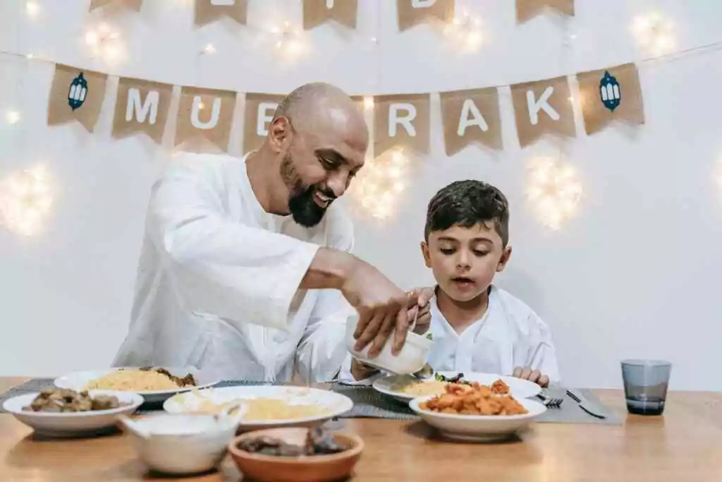 Father and son share a joyful Eid meal at a festively decorated table indoors.