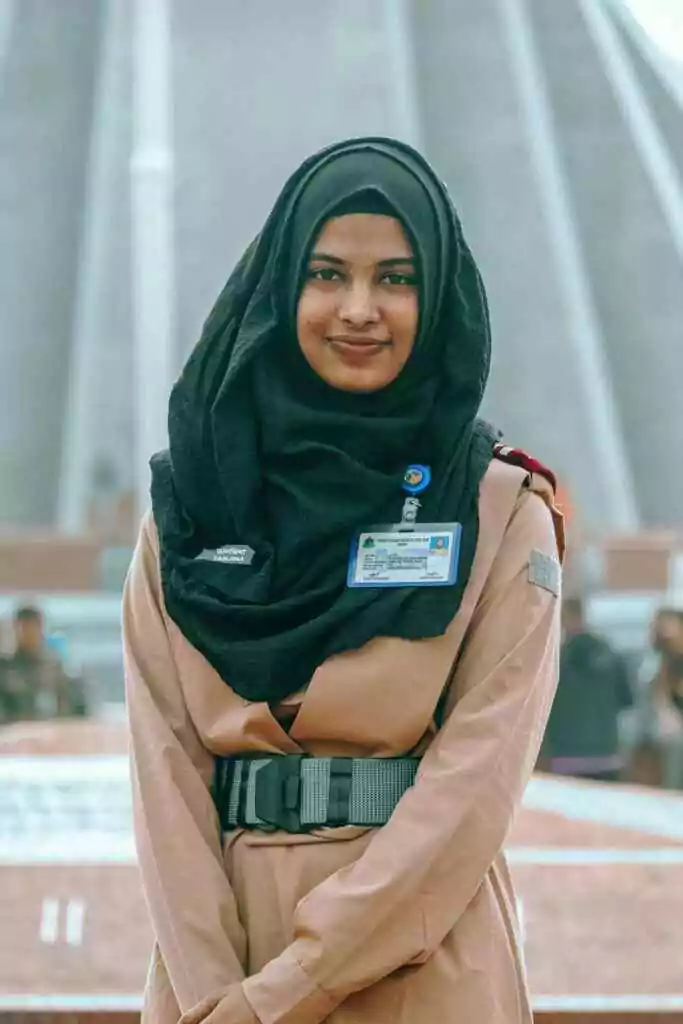 Portrait of a Muslim woman in uniform with hijab at a Dhaka landmark. Bright and confident.