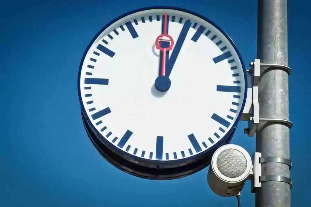 A street clock and speaker mounted on a metal pole under a clear blue sky.