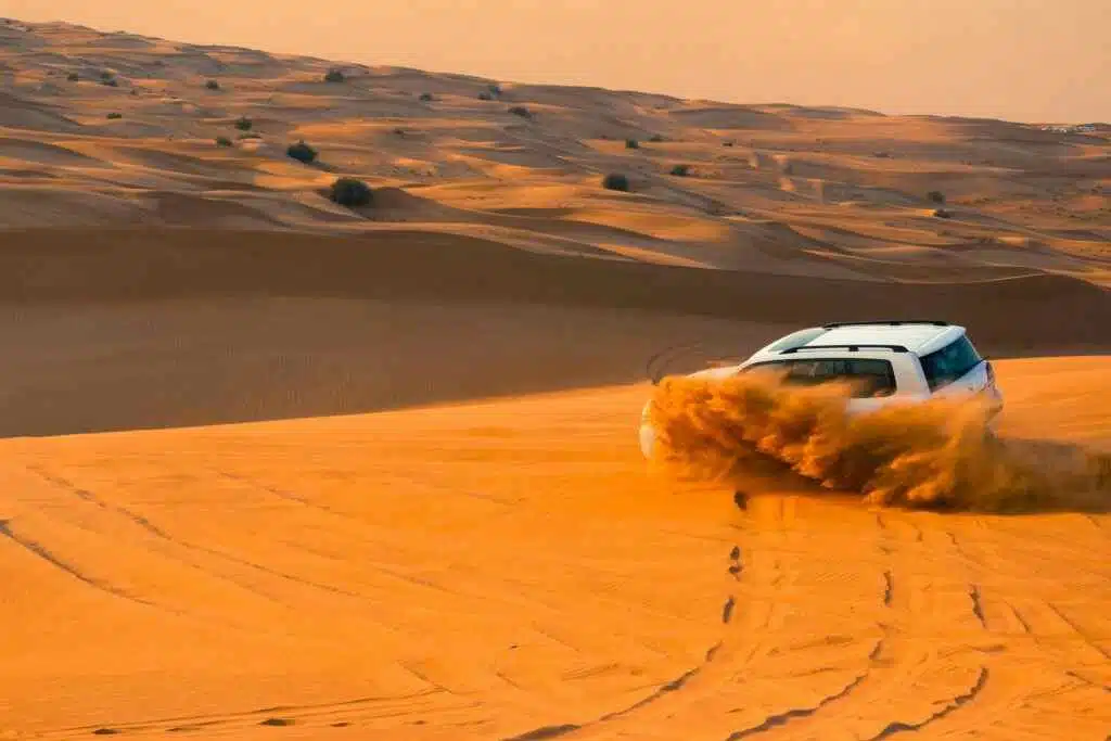 A thrilling SUV driving through the sand dunes of Dubai's desert landscape at sunset.