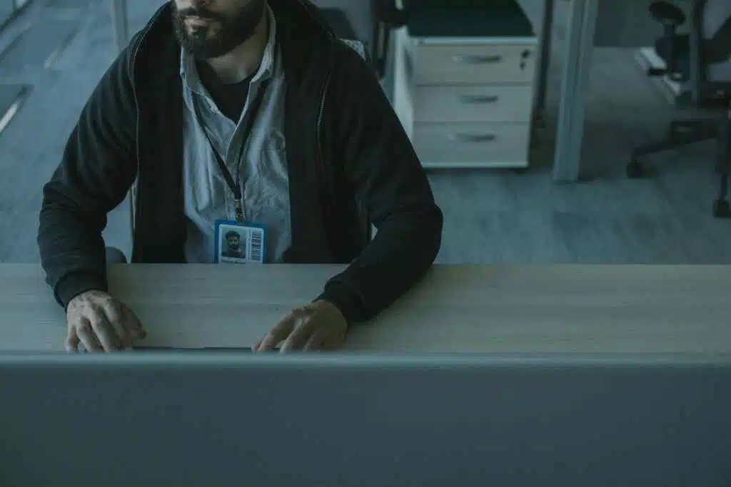A man in a black jacket works at a desk in a modern office setting.