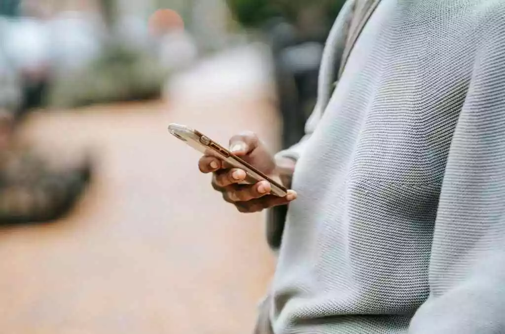 A person casually uses a smartphone outdoors in an urban environment, focusing on connection.