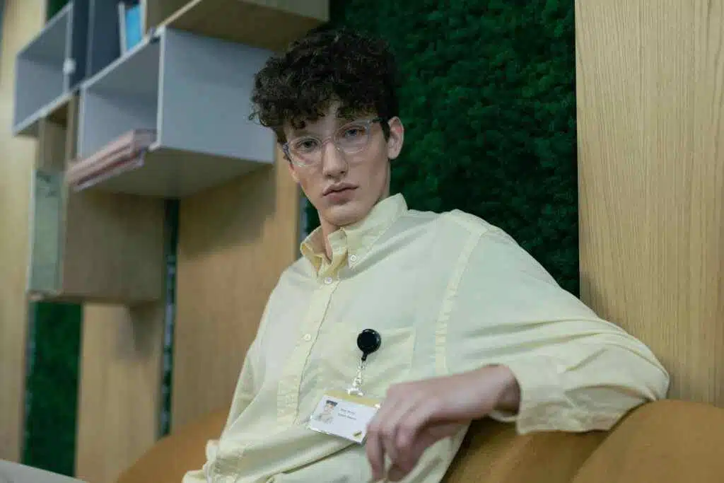 Young man in a yellow shirt with ID badge sitting in a modern office setting.