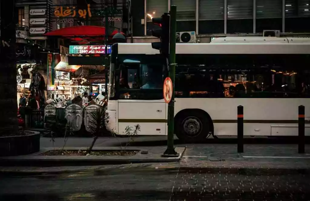 City street at night in Amman with a bus and vibrant urban life.