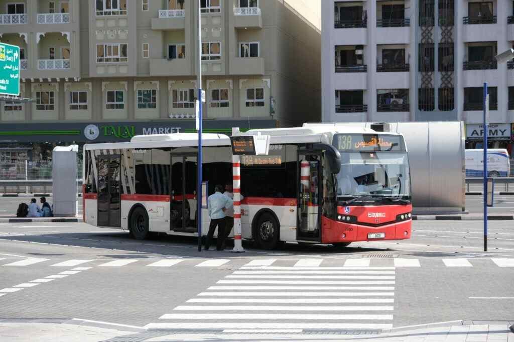 Public bus parked at a Dubai street bus stop with city buildings in the background.