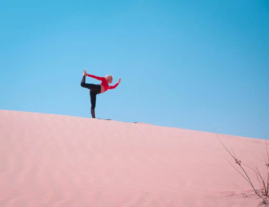 A woman practices yoga on sand dunes in Dubai, enjoying the clear blue sky and vast desert landscape.