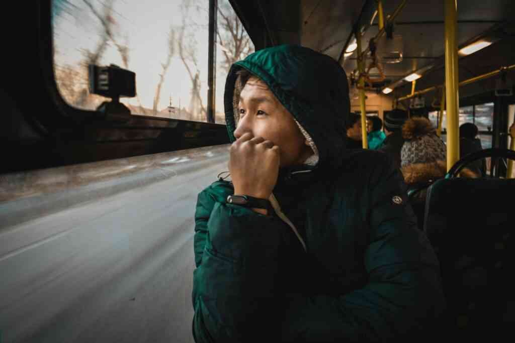 A thoughtful person in a jacket gazes out of a bus window, capturing the essence of travel.