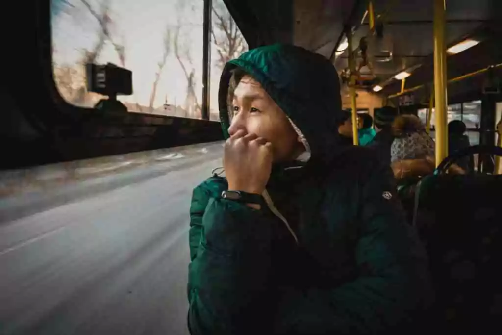 A thoughtful person in a jacket gazes out of a bus window, capturing the essence of travel.