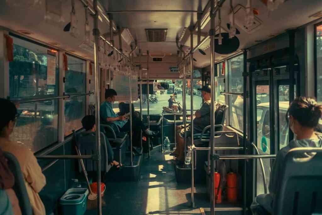Interior view of a city bus with seated and standing passengers. Urban public transportation captured during daytime.
