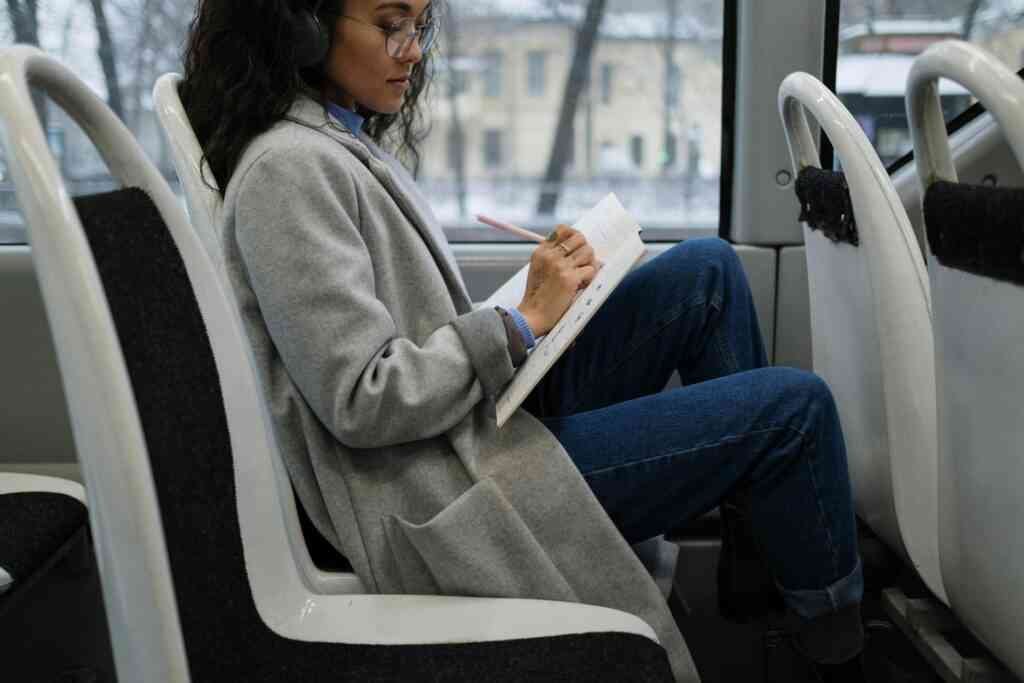 Woman writes in a notebook while listening to music on a city bus.