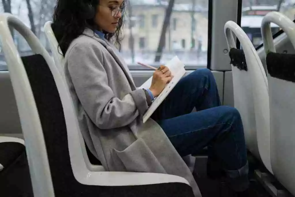 Woman writes in a notebook while listening to music on a city bus.