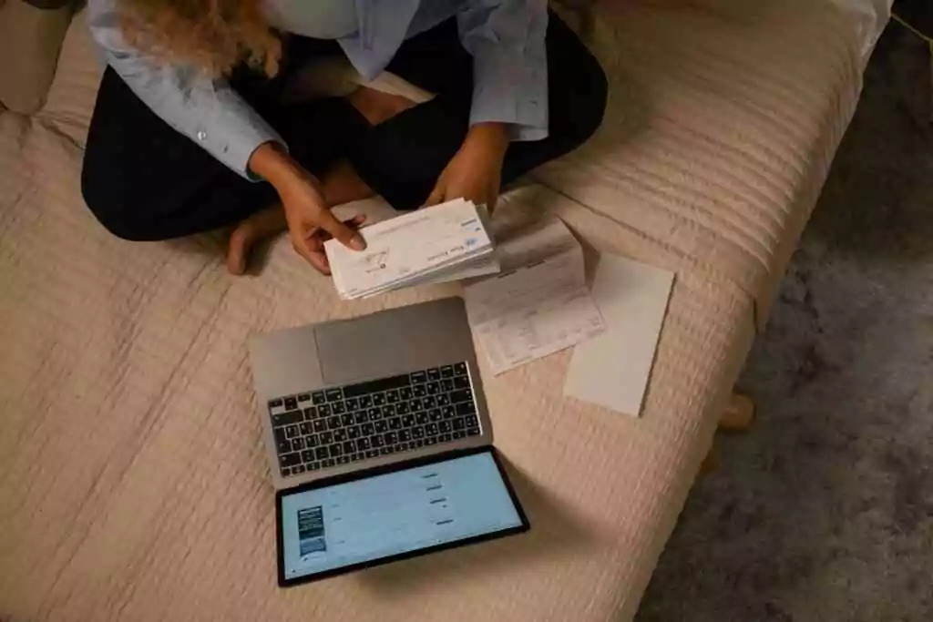 Overhead view of woman organizing finances on bed with laptop and checks.