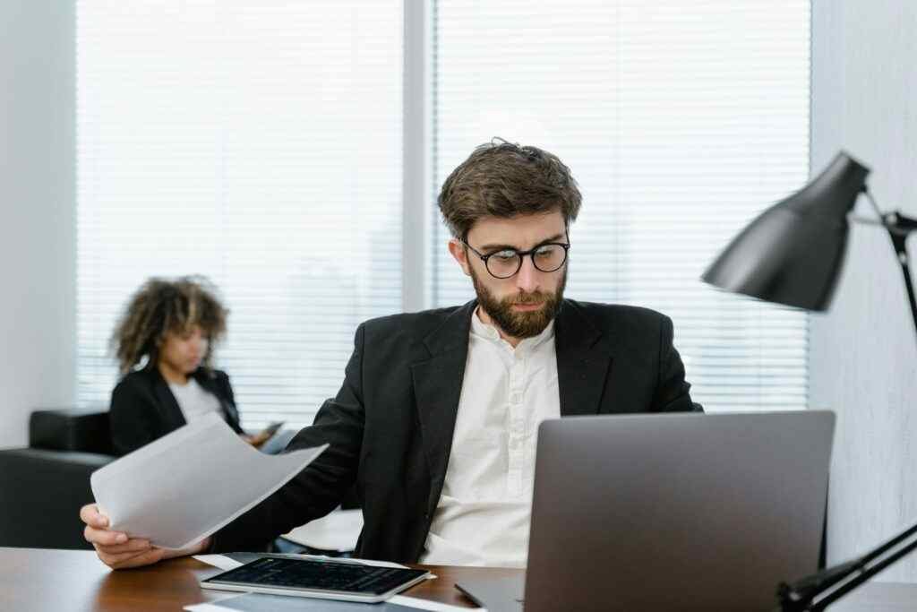 Two business professionals analyzing data on a laptop in a modern office setting, focusing on strategy.
