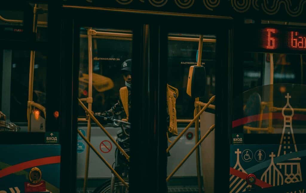 A man transporting a bicycle inside a dimly lit city bus during the night.