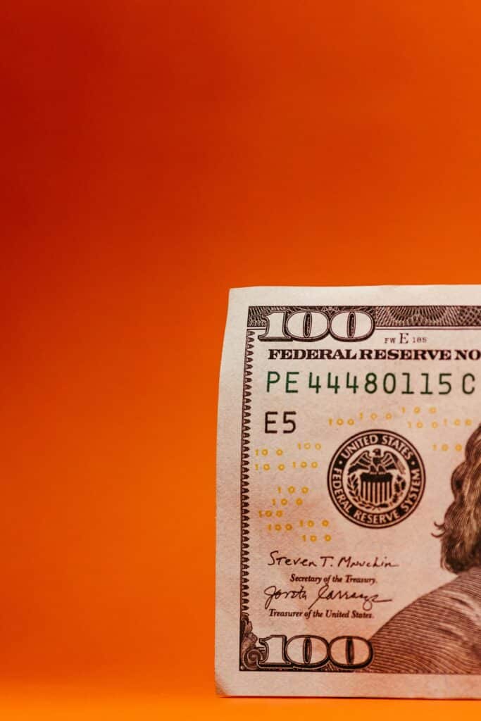 Vertical shot of a partial US 100 dollar bill against a vibrant orange background.
