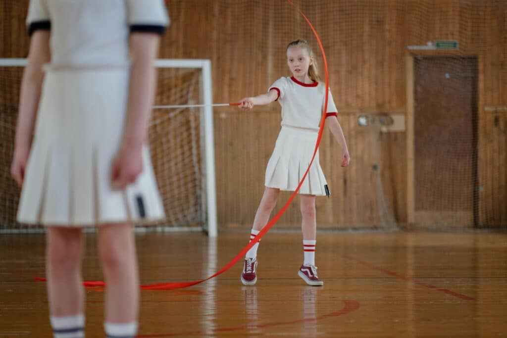 A young gymnast performs a rhythmic routine with a ribbon indoors.
