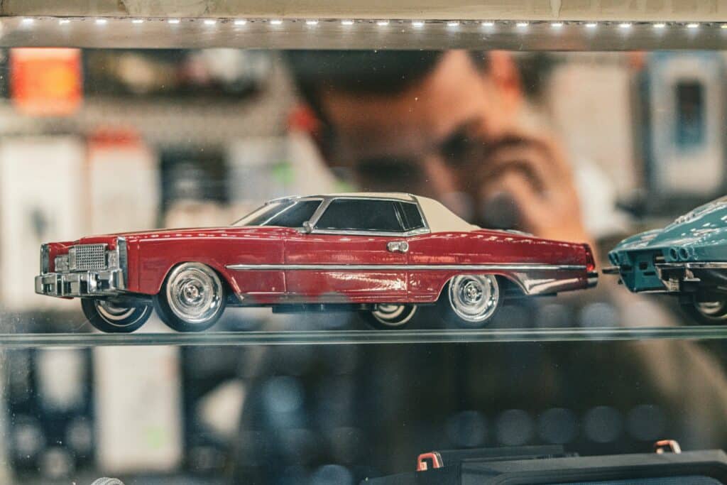 Detailed view of a vintage red model car displayed behind glass in a store setting.
