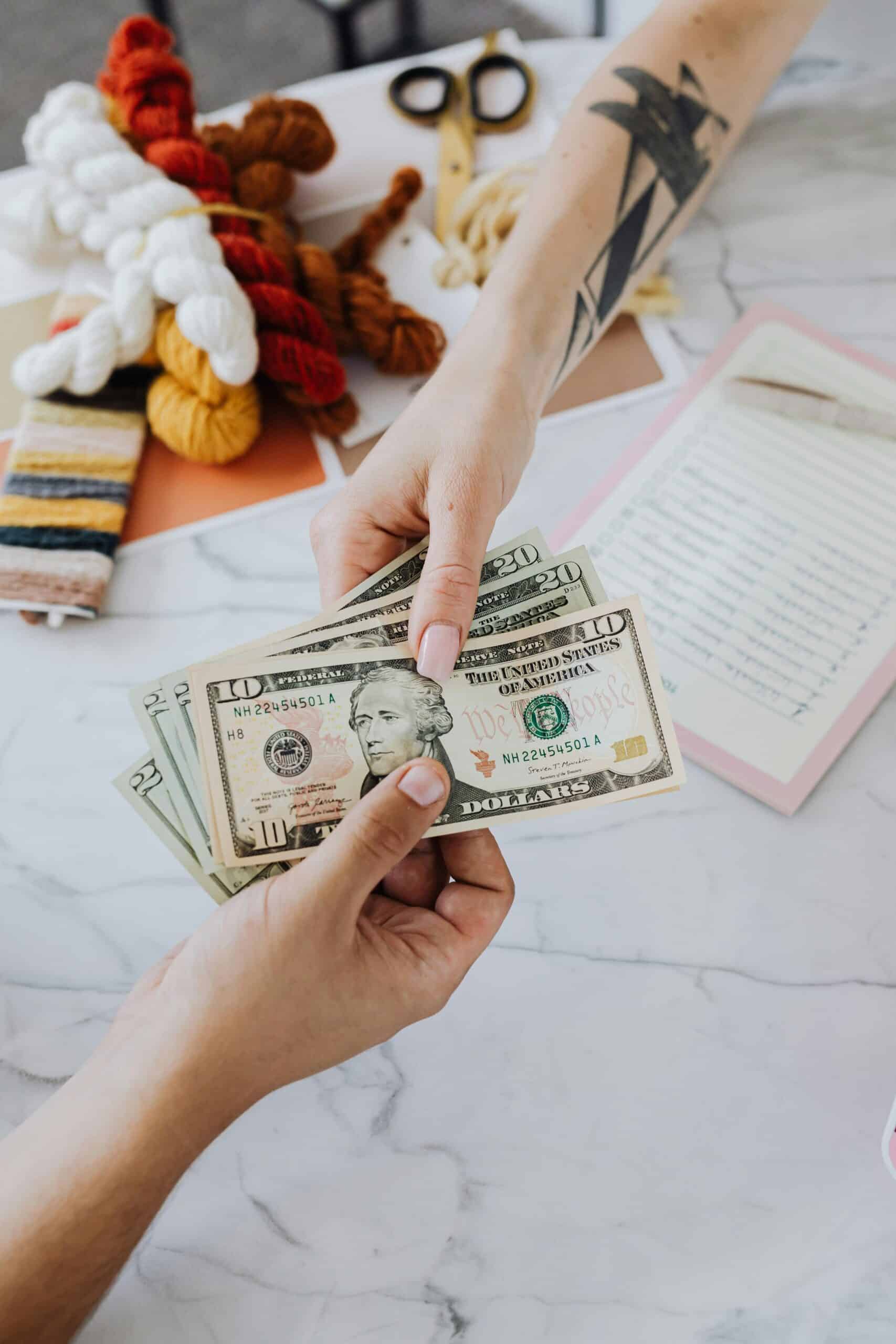 UAE PPP Calculator: Compare Salary & Cost of Living Live 2 Hands exchanging US dollars on a table with crafting supplies, highlighting financial transactions.