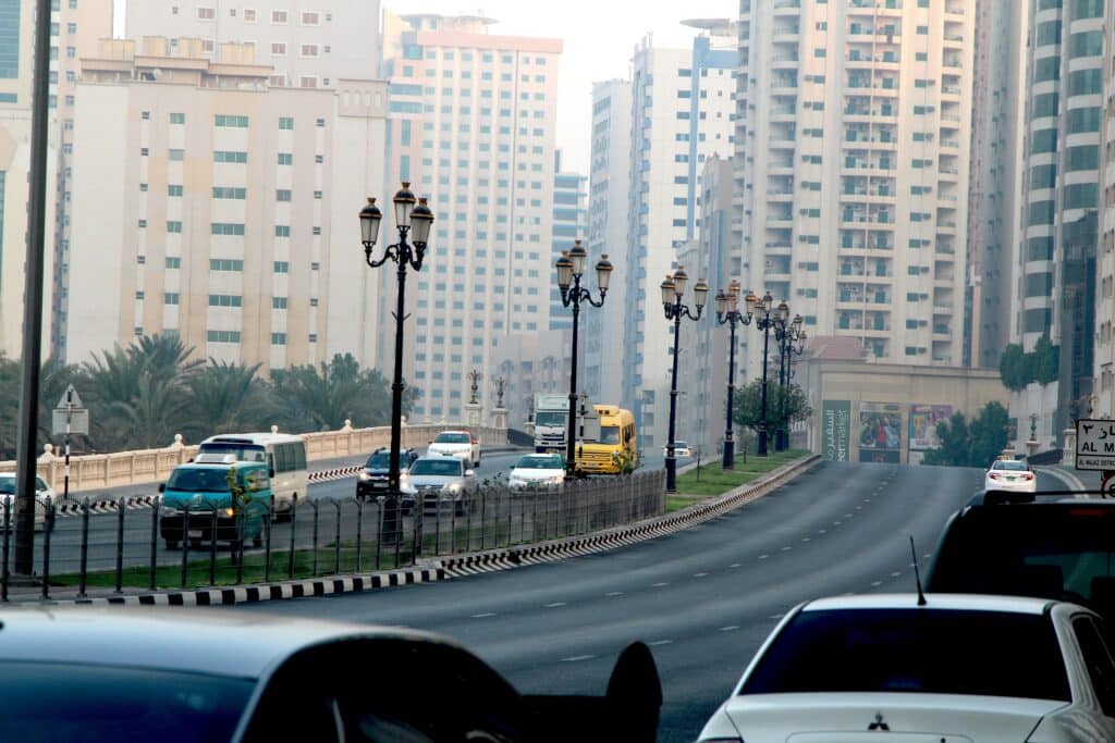 Busy street scene captured in downtown Sharjah, UAE, with modern high-rise buildings and vehicles.